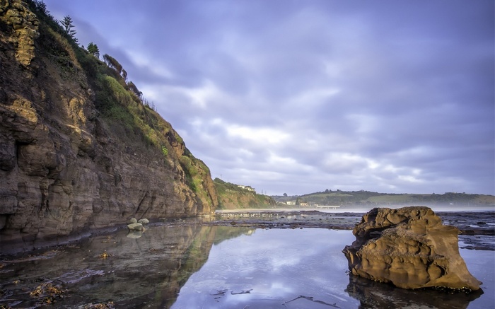 Rocky cliff face overlooking a calm ocean with a large rock in the foreground