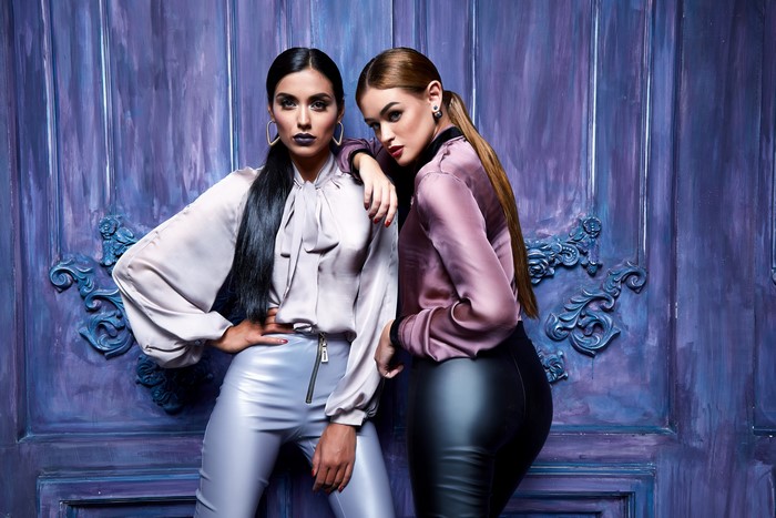 Two women in fashionable outfits posing against a purple backdrop