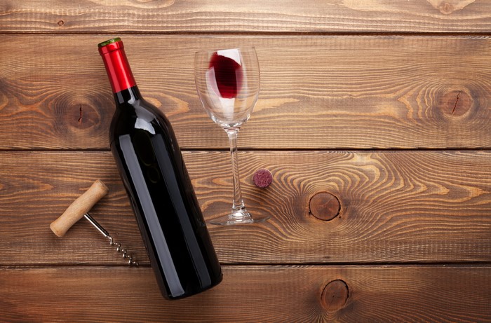 Bottle of red wine, glass, corkscrew, and cork on wood