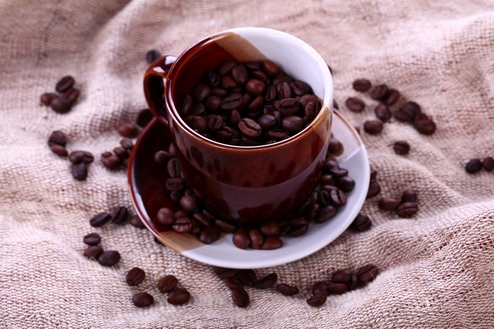 Coffee beans in a brown cup on a burlap cloth