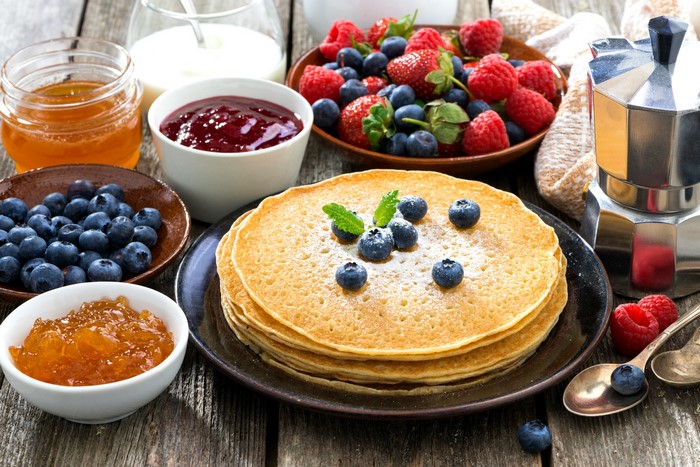 Pancakes with berries, jam, honey, and coffee maker