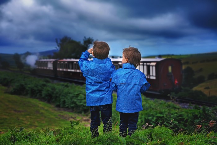 Two boys in blue jackets watching a train
