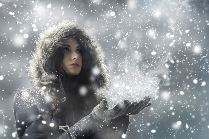 Woman in fur-hooded coat blowing snow from hands