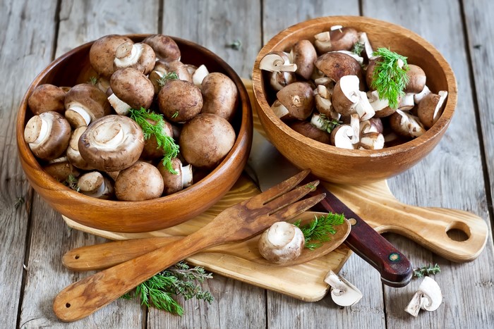 Two bowls of mushrooms with wooden utensils