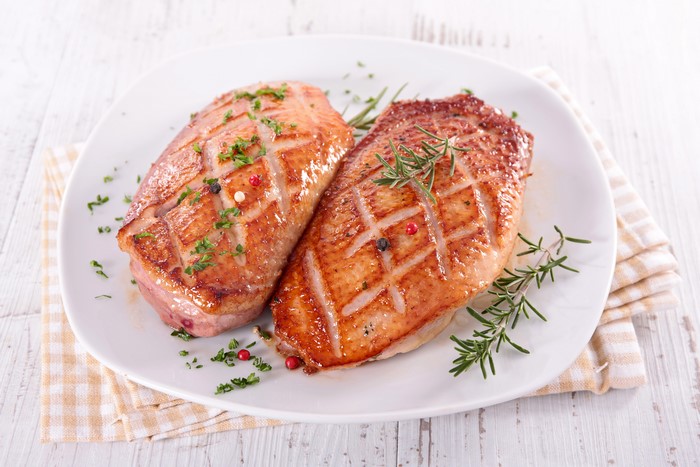 Two duck breasts on a plate with herbs