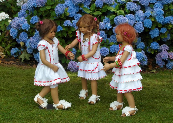 Three dolls in dresses in front of hydrangeas