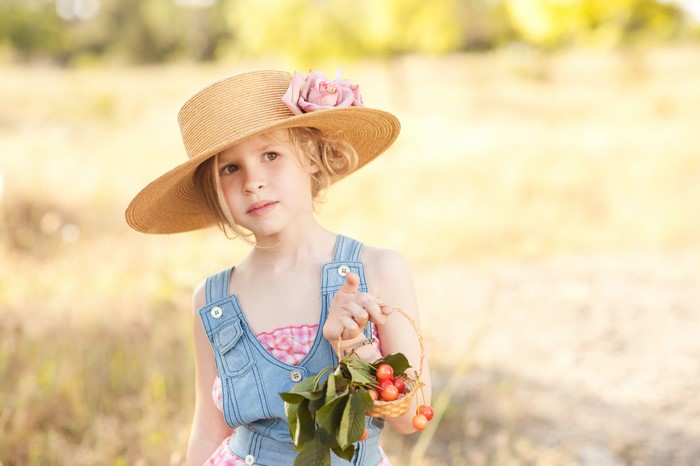 Little girl in a straw hat holding cherries