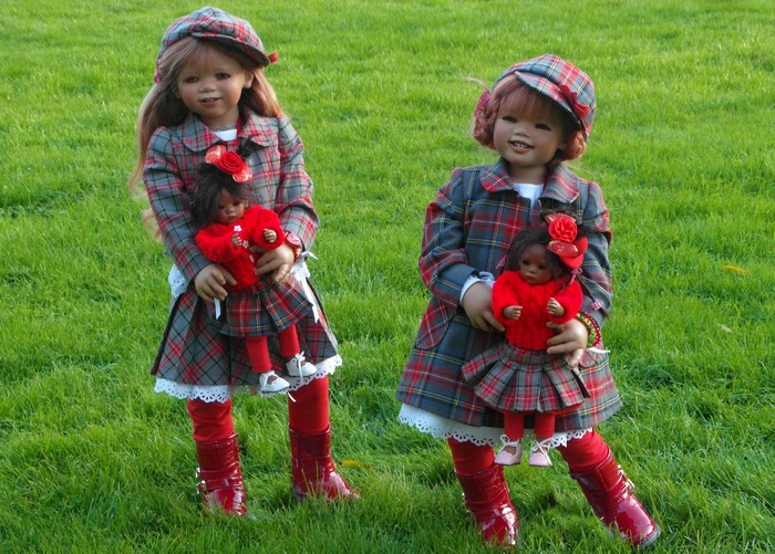 Two dolls dressed in plaid outfits holding baby dolls in a park