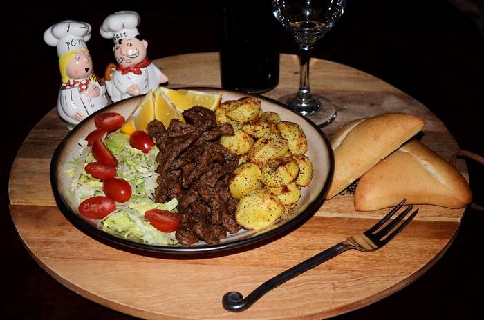 Plate of meat, potatoes, salad, and bread with salt and pepper shakers