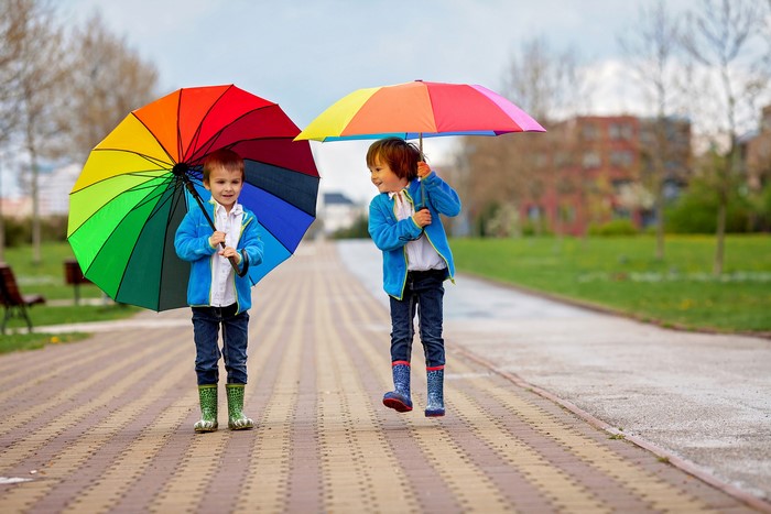 Two boys with colorful umbrellas wearing jackets and boots
