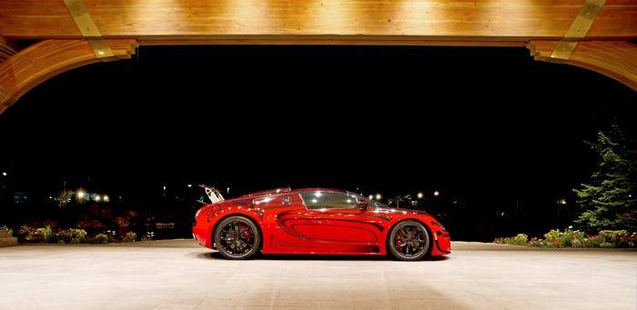 Red Bugatti Veyron parked under wooden archway at night