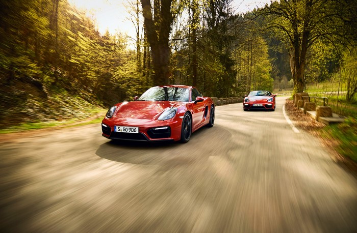 Two red Porsche cars driving on a forest road