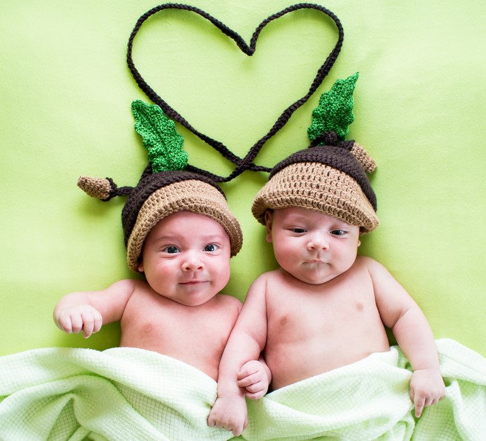 Two infants wearing acorn hats with a heart shape
