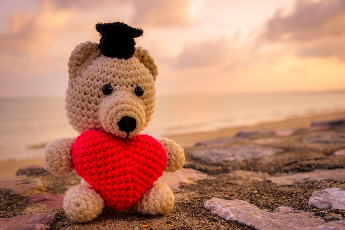 Teddy bear with heart and graduation cap on beach