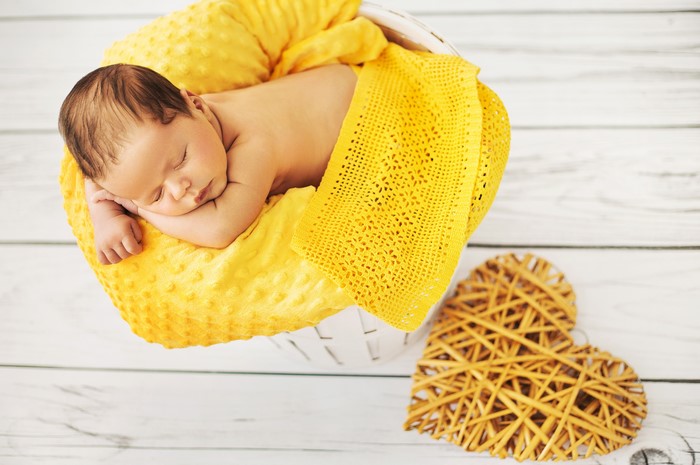 Newborn baby sleeping in a basket with yellow blanket and heart
