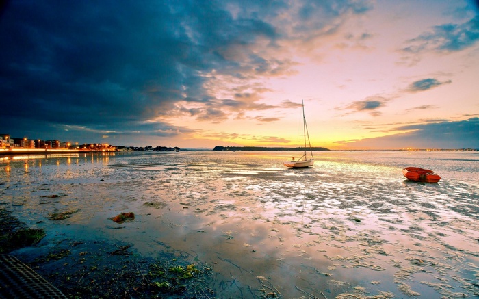 Sailboat and boat on a tidal flat at sunset