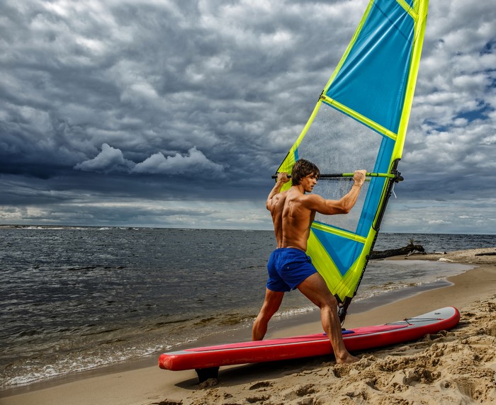 Man windsurfing on a beach with stormy clouds