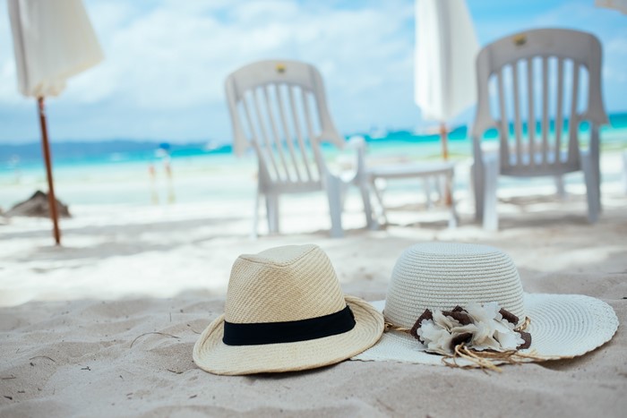 Two hats on a sandy beach with chairs and umbrellas