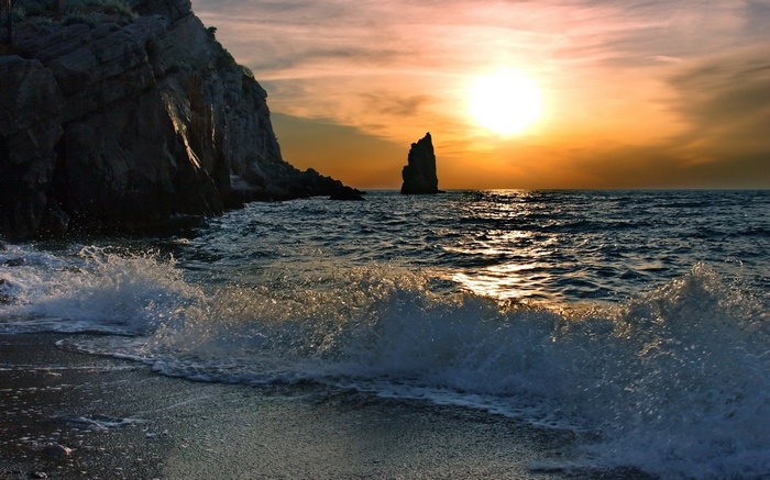 Sunset over the ocean with rocky cliffs and a sea stack