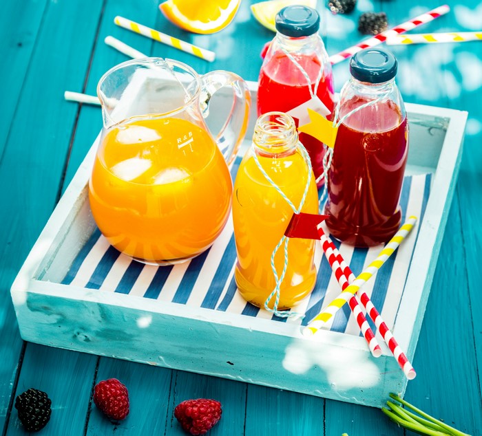 Jug and bottles of juice on a tray with berries