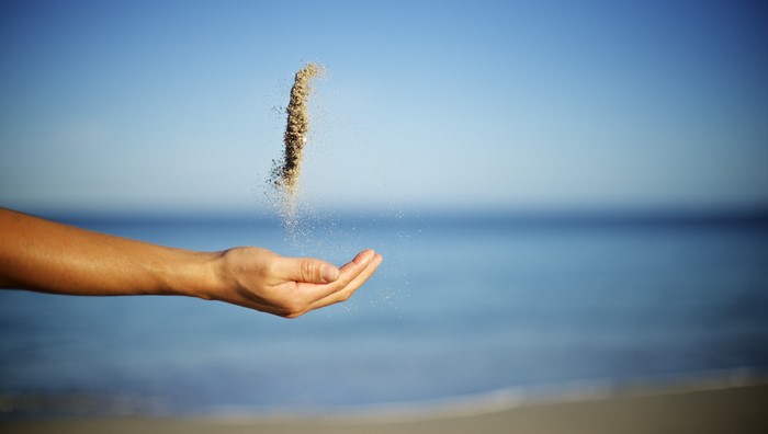 Hand pouring sand into the ocean