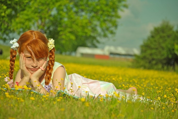 Redhead girl with braided hair lying in a field of flowers