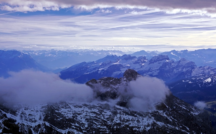 Snow-capped mountains shrouded in clouds under a streaky sky
