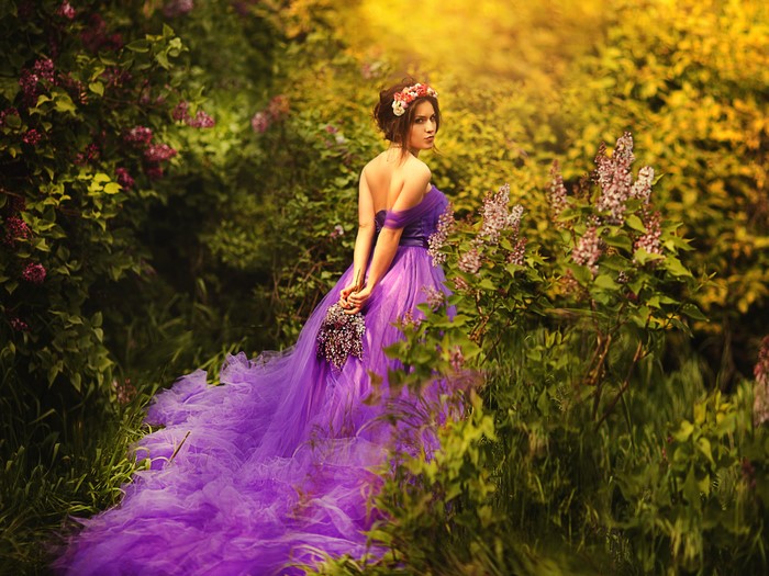 Woman in a purple dress holding flowers in a garden