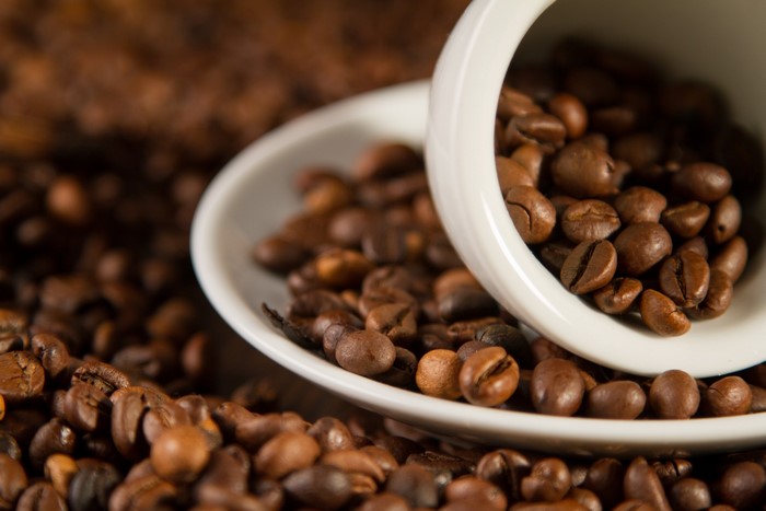Coffee beans spilling from a white cup onto a saucer