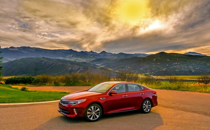 Red Kia Optima Sedan with Mountains and Sun