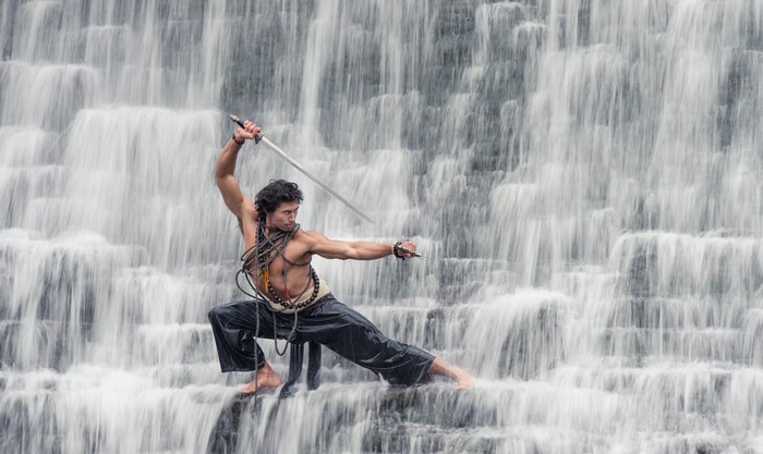 Man with sword in front of a waterfall
