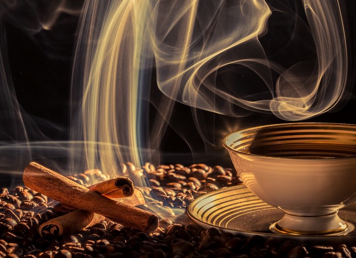 Coffee beans with cinnamon sticks and steaming cup