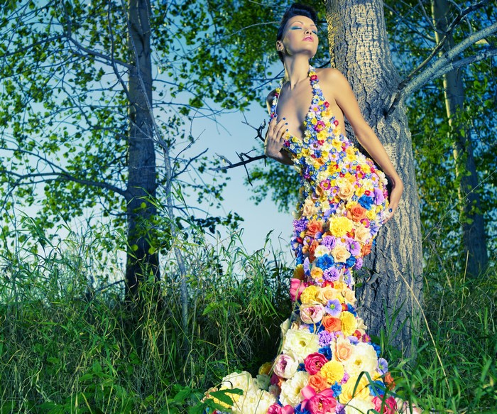 Woman in floral dress leaning against tree trunk