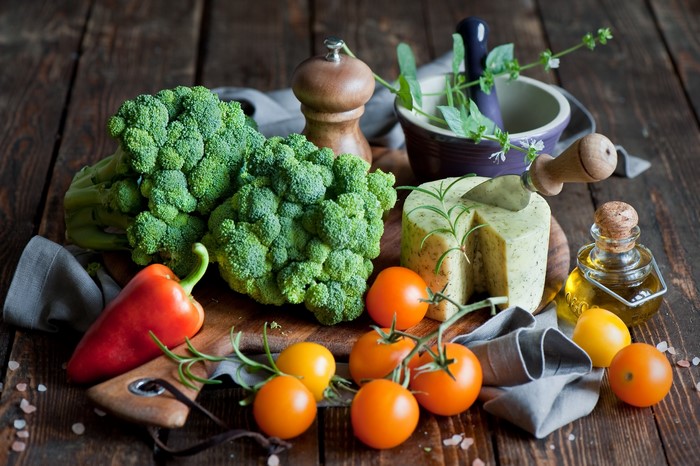 Broccoli, cheese, tomatoes, bell pepper, and olive oil on a wooden table
