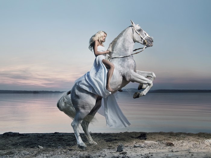 Woman in white dress riding a white horse on a beach