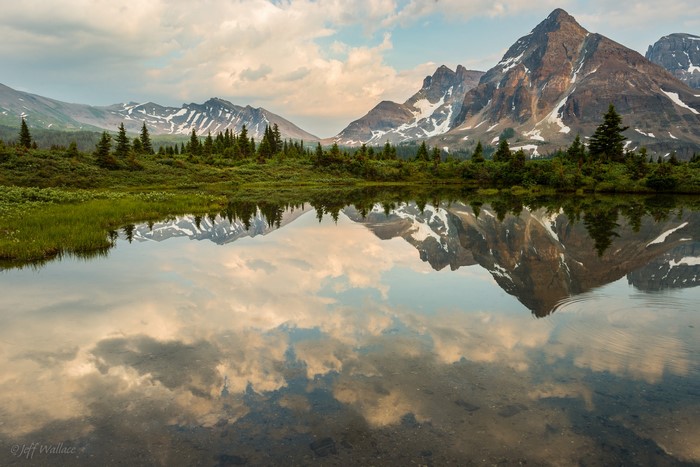 Mountains reflected in a calm lake with trees and clouds
