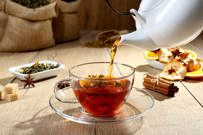 Tea being poured into a cup with spices and dried fruit