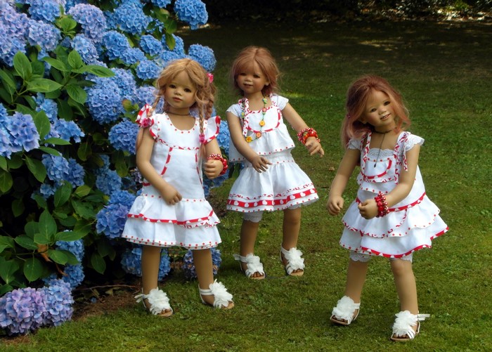 Three dolls in white dresses by hydrangeas
