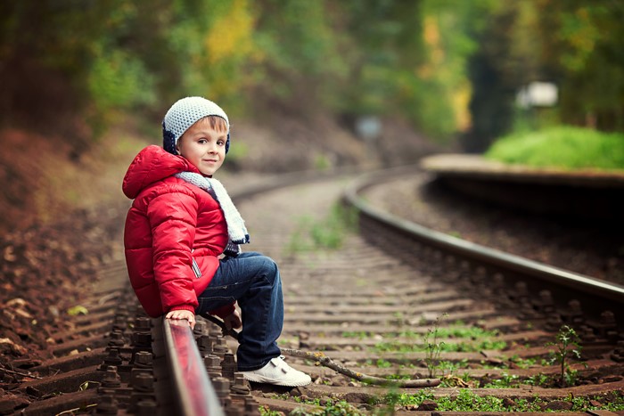 Boy in Red Jacket Sitting on Railroad Tracks