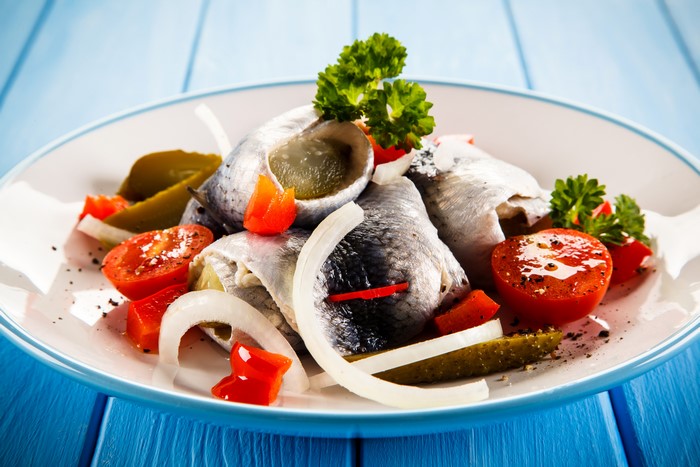 Herring rolls with tomatoes, onions, and pickles on a plate