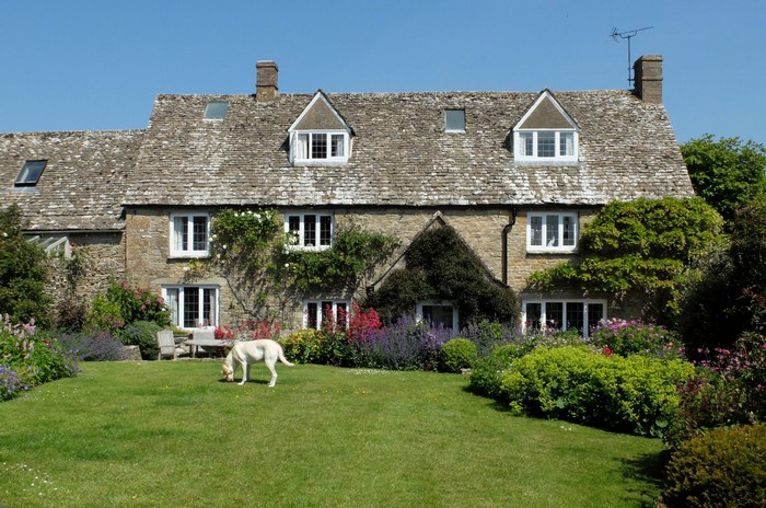 Stone cottage with a dog on a lawn in the Cotswolds