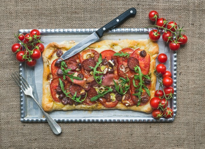 Rectangular pizza with tomatoes, sausage, and arugula on a tray