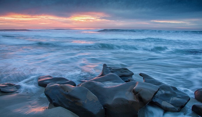 Sunset over the ocean with rocks on the shore