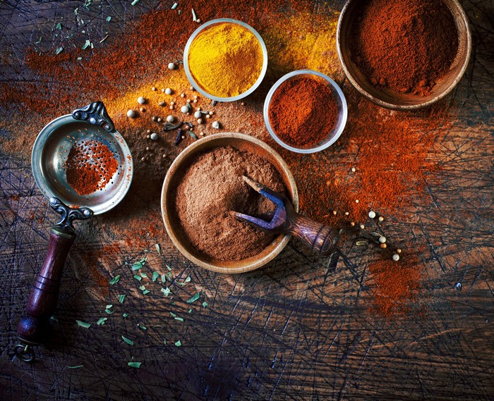 Spices in bowls and sieve on wooden surface