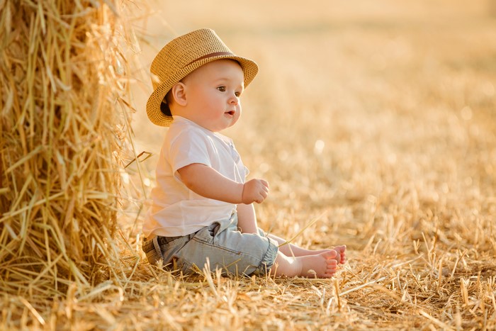 Baby in straw hat sitting in hay