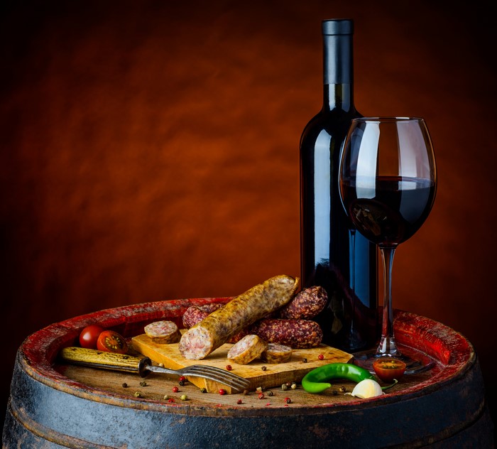Wine bottle and glass with sausages on a barrel