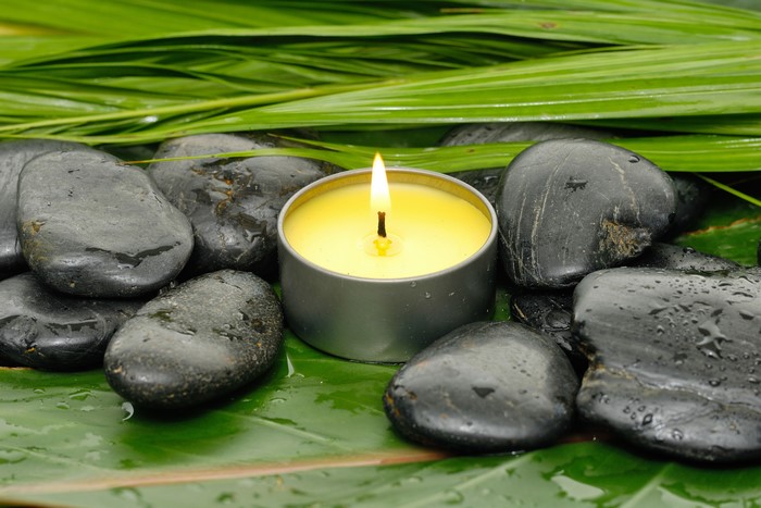 Spa stones and lit candle with green leaves
