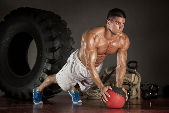 Man performing medicine ball push-ups with large tire