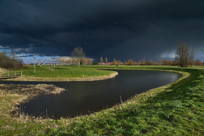 Dark Thunderclouds over a Dutch Landscape with a Pond