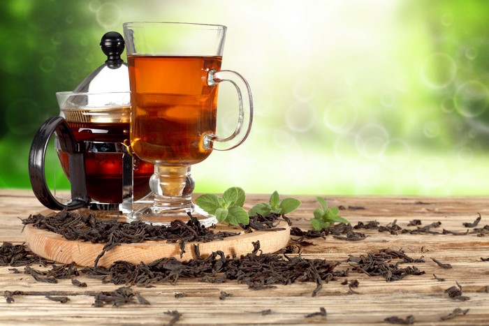 Tea in a glass mug and teapot with dried tea leaves and mint